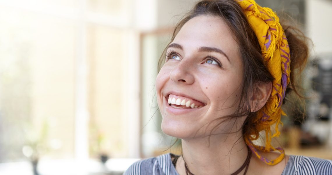 Elegant bright woman wearing scarf on head having brown shining eyes and broad smile with white even teeth looking up with happy expression. Excited student girl enjoying good vacations at home